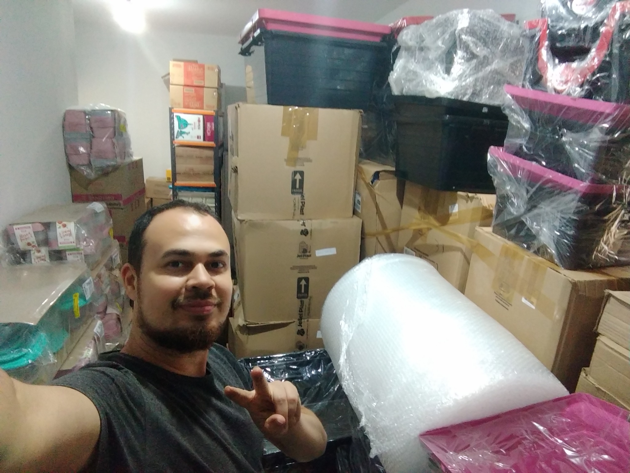Marcos em uma selfie no espaço de estoque, junto a caixas, potes e materiais de embalagem.